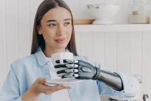 Confident handicapped girl holding cup of tea with cyber hand. Happy woman with makeup is smiling. photo