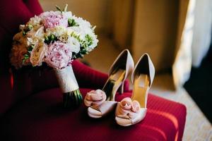 Brides shoes and wedding bouquet with gentle flowers on red chair. Wedding preparation. Wedding accessories. Pink brides shoes and lush bouquet in brides room. Brides morning. Wedding photo