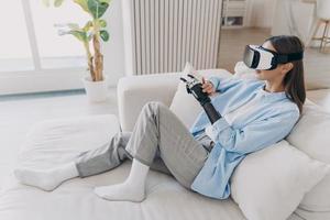 Disabled girl relaxing in vr glasses on couch. Handicapped person setting functions of cyber arm. photo