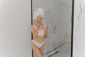 Image of beautiful young girl with towel on head holding moisturizing face cream photo