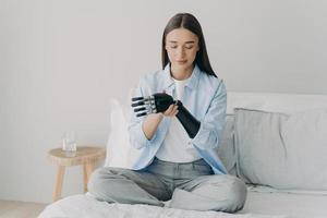 Disabled young woman is assembling electronic control prosthesis. Artificial arm adjusting. photo