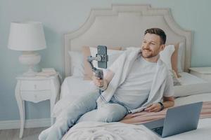 Young man lying  on bed while video chatting using phone photo