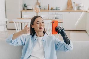 Handicapped confident woman has video call on smartphone. Girl is holding phone with artificial arm. photo