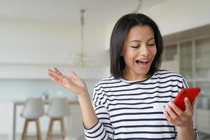 Happy astonished woman holds phone, reads good news in mobile app, celebrates success, job promotion photo