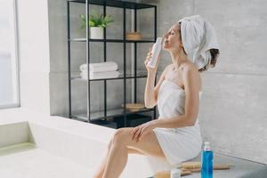 Slim european girl takes a smell of body lotion from bottle and relaxing in bathroom at home. photo