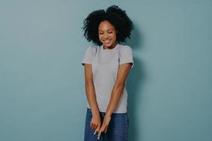 joven africana mirando hacia abajo con una expresión de cara tímida y tímida, aislada sobre fondo azul foto