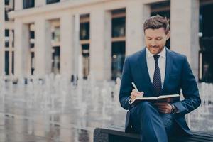 trabajador de oficina vestido formalmente organizando su día en un cuaderno mientras trabaja al aire libre foto