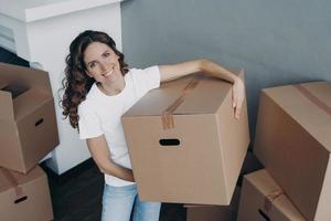 Happy hispanic woman purchasing real estate and unloading cardboard boxes alone in new apartment. photo