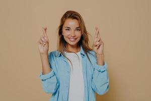 Positive lady with fingers crossed on beige background photo