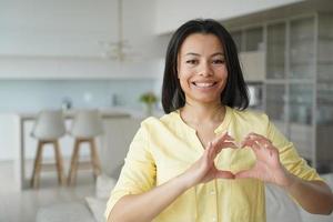 mujer sonriente muestra gesto de corazón, signo de amor, apoyo, gratitud en casa. caridad y donacion foto