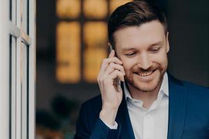 feliz y elegante hombre de negocios hablando por teléfono móvil con placer foto