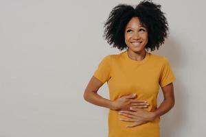 feliz mujer afroamericana riéndose a carcajadas de una broma hilarante, manteniendo las manos en el estómago foto