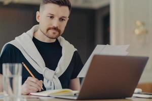 Busy businessman using laptop and making some notes at his workplace photo