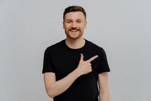 Young positive man pointing at upper right corner with pleased face expression photo