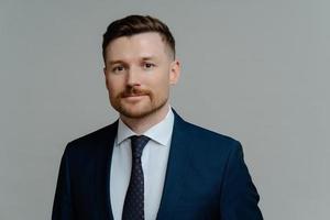 Young handsome male executive manager in elegant suit posing against grey background photo