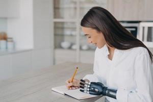 School girl with bionic prosthesis is studying or working remotely and taking notes at the desk. photo