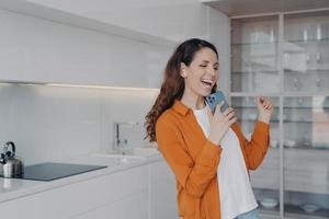 feliz mujer europea está cantando con teléfono como con micrófono. canción favorita cantando en casa. foto