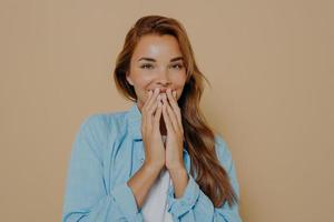 Giggling woman covering her mouth with hands on beige background photo