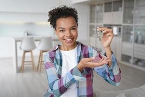 una chica afroamericana despreocupada sostiene la llave de la casa y sonríe. adolescente feliz es dueño de casa. foto