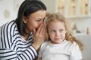 Mother or babysitter whispering sharing secret with kid daughter. Trusting relationship, friendship photo