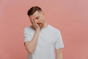 Young exhausted caucasian man posing against pink background photo