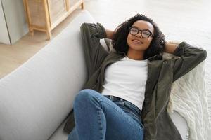 Relaxed biracial teen girl in glasses rest, lying on couch, enjoy break on sunny weekend at home photo