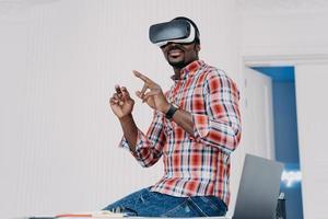 Happy african american guy in vr goggles at home. Freelancer .working on futuristic design project. photo