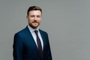 Confident male CEO in formal outfit has good business reputation looks smart at work isolated over grey studio backgrounf with copy space for your promotion. Charismatic employer poses indoor photo