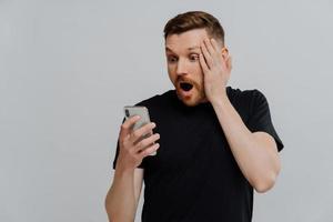 Impressed man reading stunning news on smartphone with shocked expression photo