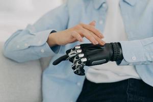 Girl is setting up her bionic hand and pressing buttons. Young woman with artificial arm at home. photo