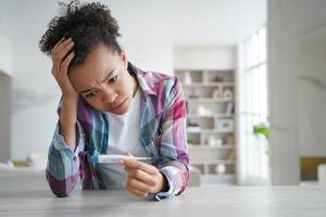 Anxious girl gets positive pregnancy test result. Young woman is holding stripe test. photo