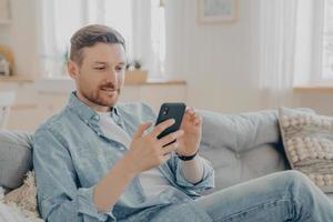 joven sentado en el sofá y navegando por la web en su teléfono foto