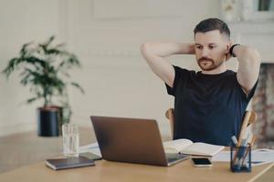 Male entrepreneur looking at laptop screen and relaxing while working in modern office photo