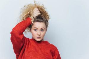 Indoor shot of beautiful blue eyed female in red sweater, poses with stunned expression, dressed in red sweater, isolated over white background. Wondered young woman doesnt believe in something photo