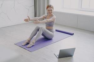 Slim girl in sportswear stretching on mat at home. Online personal training and distance learning. photo