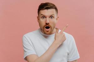 Shocked young man pointing with finger to side with surprised face expression photo