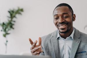 Smiling african american businessman holding a video call with customers on laptop, advises clients photo