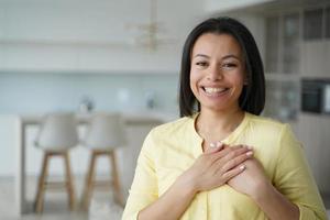 una mujer sonriente y agradecida se toma de la mano en el pecho siente gratitud, aprecia la ayuda, una buena obra en casa foto