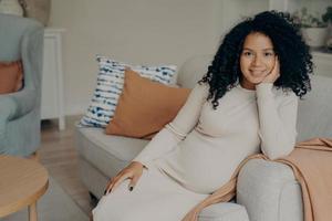 Beautiful african expectant mother sitting in relaxed pose in living room photo