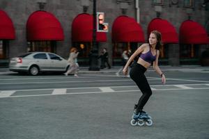 Full length shot of active slim young woman dressed in sportsclothes rides on rollers to strengthen arms and legs muscles improves balance agility and coordination has good mood burns calories photo