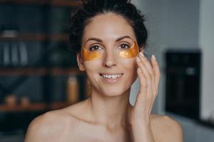 Face of young woman which applies collagen eye patches. Portrait of happy girl doing spa procedures. photo