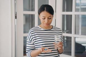 Pensive woman holds pills doubting whether to take medicines at home. Healthcare, self-medicating photo