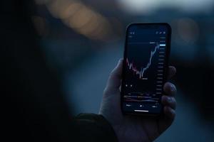 Trader holding smartphone with financial chart and analyzing price flow on stock market photo