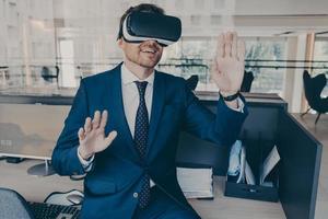 Excited entrepreneur in virtual reality glasses touching objects interact with 3D simulation photo