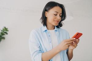 mujer española feliz está enviando mensajes de texto en el teléfono inteligente y sonriendo. mensajes sms leer y escribir. foto