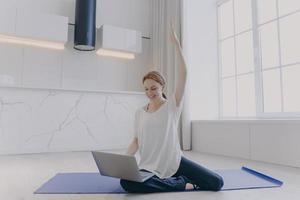 Young woman sitting on her knees on floor with laptop. Online fitness tutorial. Distance training. photo