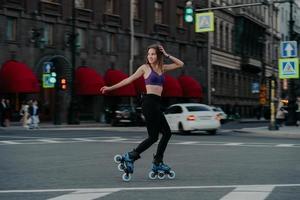Outdoor shot of sim woman rides on rollerblades loks away trains different muscle groups of legs and core develops endurance manages her weight burns calories improves balancing. Cardio workout photo