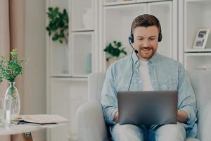 Smiling bearded guy chatting online with friend at home photo