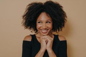 Studio shot of happy Afro girl keeps hands together under chin photo