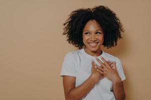 Portrait of happy african woman posing with smile looking away, holding hands on chest photo